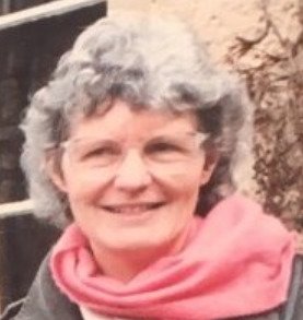 En gråhårig kvinna med glasögon och rosa halsduk.