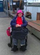 En kvinna i rosa hatt som sitter i rullstol. 