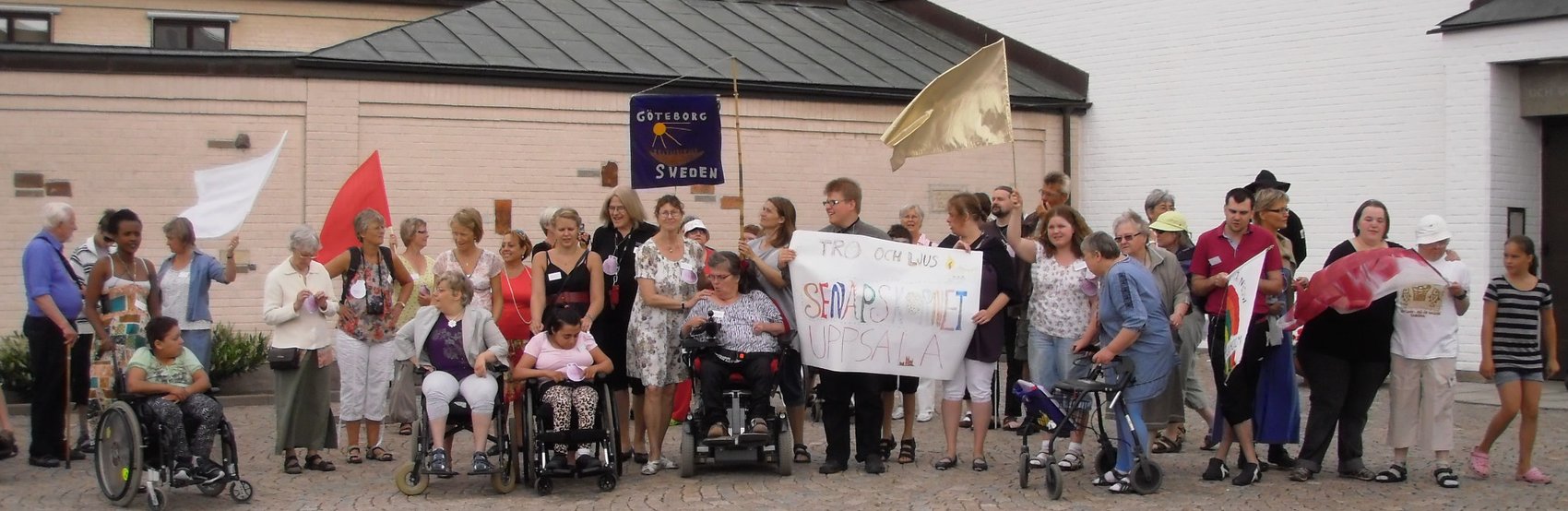 Människor i olika åldrar som står med banderoller utanför en kyrka